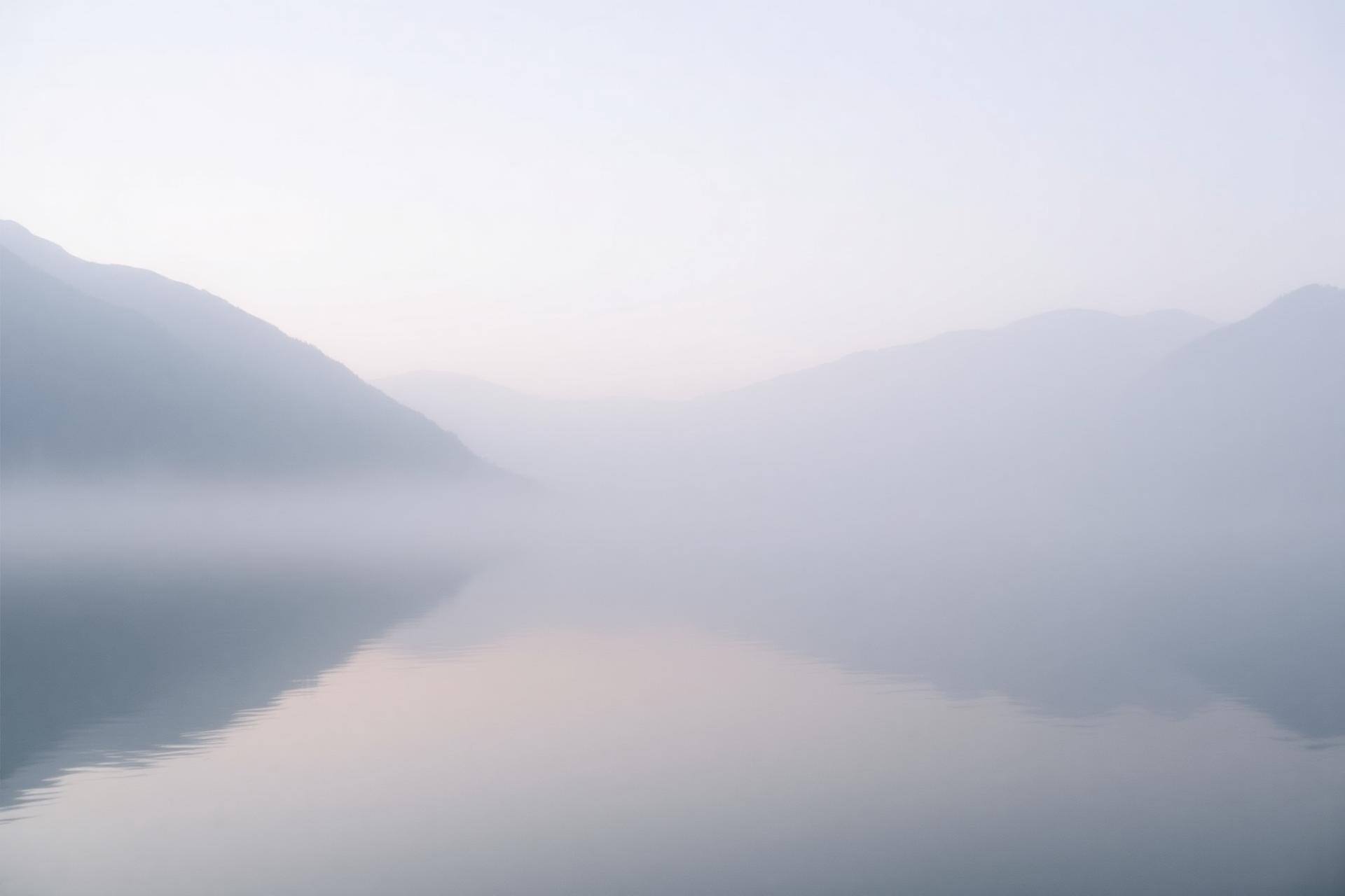 A still lake at dawn, mist drifting between distant mountains